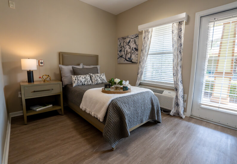 Resident Bedroom with Patio Door and Neutral Decor for Seniors at Assisted Living Facility Resident Bedroom with Patio Door and Neutral Decor for Seniors at Assisted Living Facility
